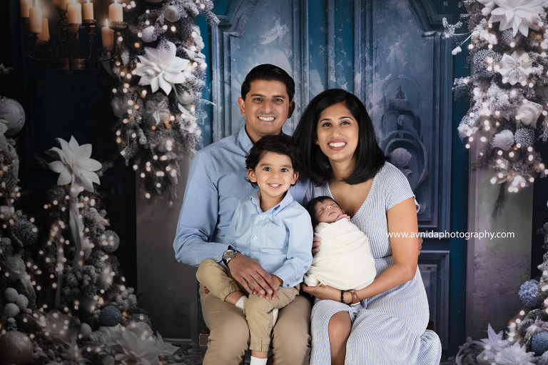 Step into a winter wonderland filled with laughter and love as a family poses in front of a picturesque blue door with festive cheer. Avnida Photography captures the magic of the holidays with timeless family portraits
