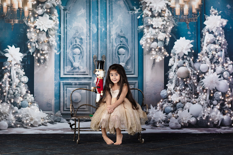 A child's eyes widen with amazement as they stand beside a nutcracker soldier, the vibrant blue door serving as a magical backdrop. Avnida Photography captures the innocence and excitement of the holiday season in this heartwarming portrait
